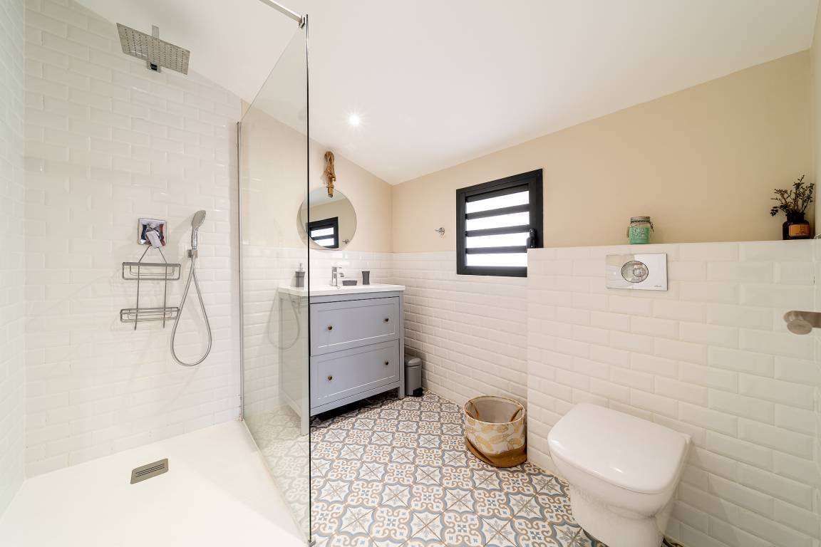Salle de bains blanche avec douche à l’italienne, vasque et carreaux à motifs