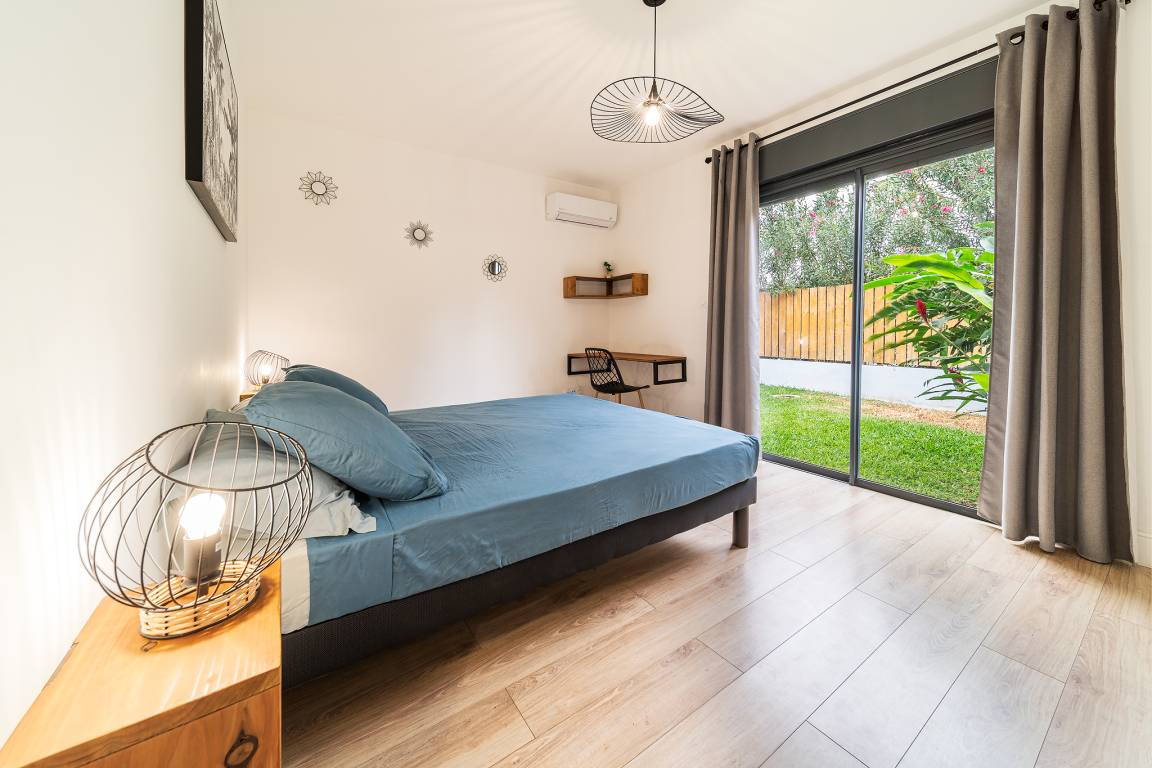 Chambre avec lit double bleu et baie vitrée donnant sur le jardin tropical